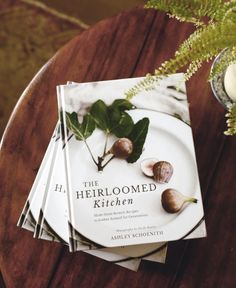 three cookbooks sitting on top of a wooden table next to a vase with flowers