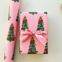 a pink wrapping paper with christmas trees on it next to a pair of scissors and a pen