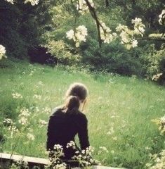 a woman sitting on a bench in the middle of a field with wildflowers