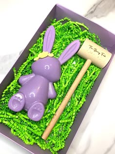 a cake in the shape of a purple bunny with a wooden stick and green grass