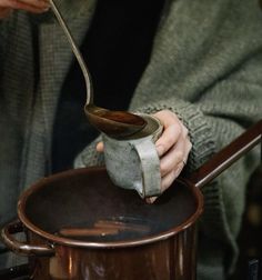 a person pouring something into a pot with a ladle in their hand and a wooden spoon sticking out of it