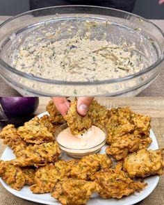 someone dipping something into a bowl of dip and some fried food on a white plate