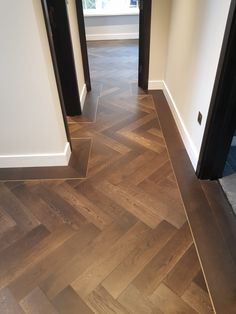 an empty hallway with wood flooring and white walls, leading to two black doors