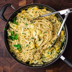 a pan filled with pasta and vegetables on top of a wooden table