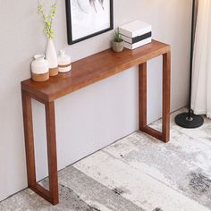 a wooden table with two vases on it next to a white wall and a black lamp