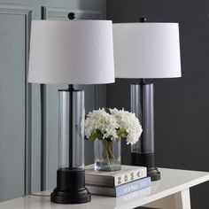 two lamps sitting on top of a table next to a book and vase with flowers