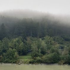 a boat is on the water in front of some trees and foggy skies above it