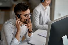 two people sitting at a desk with a computer and headphones in front of them