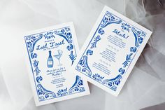 two blue and white wedding menus with wine glasses on them sitting next to each other