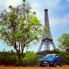 a blue car parked in front of the eiffel tower with trees around it