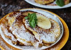 powdered sugar covered pancakes with bananas and mint sprinkled on top are sitting on a yellow plate