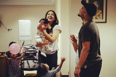 a group of people standing around each other in a living room with one woman holding a baby