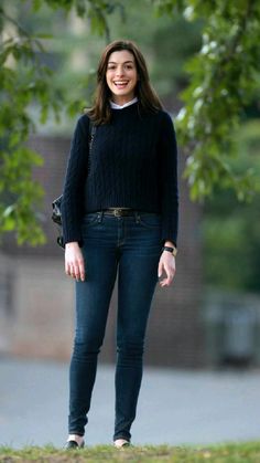 a woman in black sweater and jeans standing under a tree with her hand on her hip