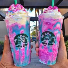 two people holding up drinks with pink and blue swirled toppings