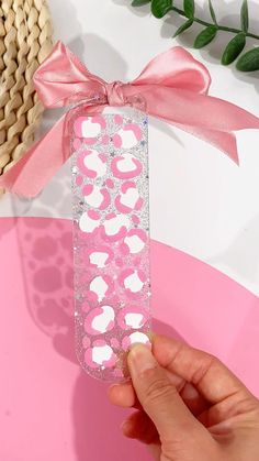 a hand is holding a pink and white box with hearts on it, next to a plant