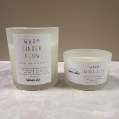 two candles sitting next to each other on top of a white tablecloth covered counter