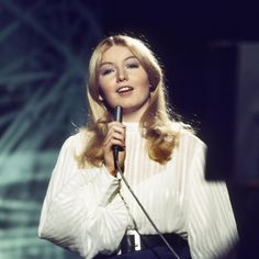 a woman holding a microphone in her right hand and wearing a white shirt on stage