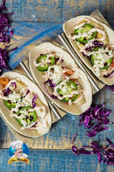 four tacos with different toppings sitting on a blue table next to purple flowers