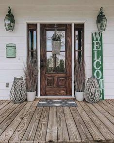 a wooden porch with potted plants on it and welcome sign above the front door