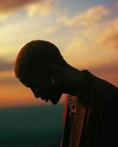 a man with his head down looking at his cell phone in front of the sunset