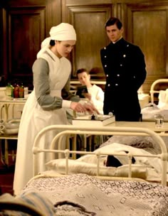 a man and woman standing next to each other in a room with beds, hospital gowns