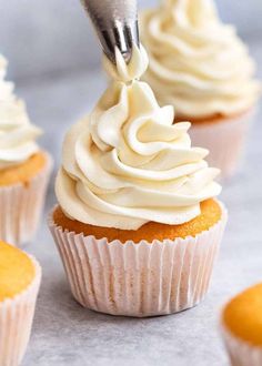 a cupcake being frosted with white icing by a piping tool on top of the cupcakes