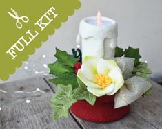 a white candle sitting on top of a red container filled with holly leaves and flowers