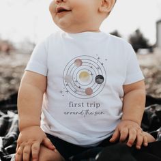 a baby sitting on top of a blanket wearing a t - shirt that says first trip around the sun