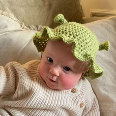 a baby wearing a green crocheted hat on top of a couch