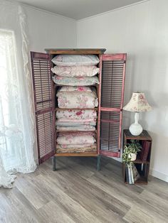 a wooden shelf filled with lots of pillows next to a lamp on a side table