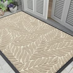 a beige and black area rug with leaves on the front door mat, next to potted plants