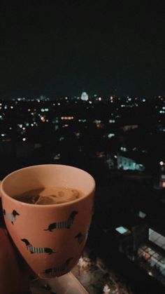 a person holding a cup of coffee in front of a cityscape at night