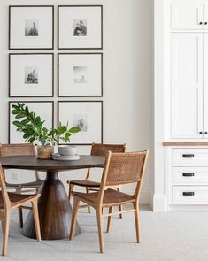 a dining room table with four chairs and pictures on the wall behind it, along with two potted plants