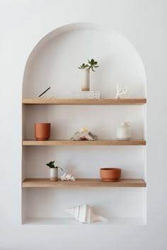 three wooden shelves with plants and vases on them in a white walled room by the wall