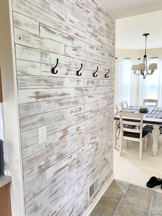 a dining room table and chairs in front of a wooden wall with hooks on it