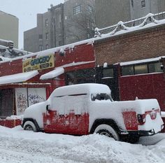 a red truck parked in front of a building covered in snow