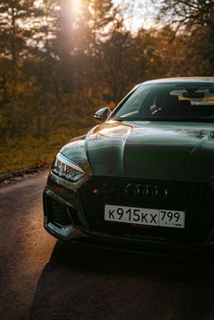 the front end of a green car parked on a road with trees in the background