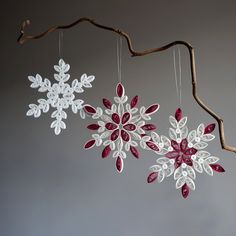 three snowflakes hanging from a tree branch with red and white decorations on them