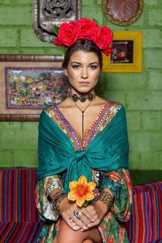 a woman sitting on top of a couch wearing a green dress and red flowers in her hair