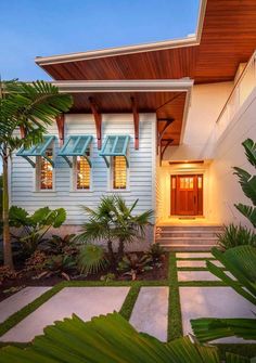 a white house with blue shutters and palm trees in the front yard at dusk