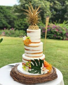 a three tiered cake with pineapple and flowers on top sits on a table outdoors