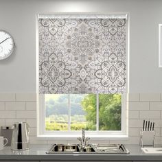 a kitchen window with roman blinds and a clock on the wall