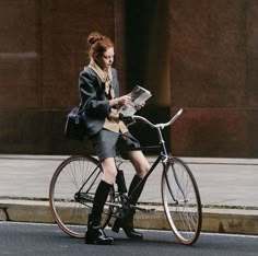 a woman sitting on top of a bike while reading a newspaper