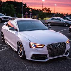 a white car parked in a parking lot with other cars behind it at sunset or dawn