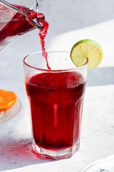 a glass filled with red liquid next to an orange and lime wedged into it