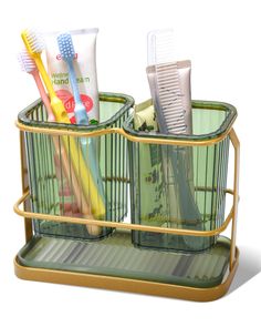 three toothbrushes and two toothpaste tubes in a metal holder on a white background