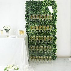 there is a tall green wall with wine glasses on it and flowers in vases next to the table