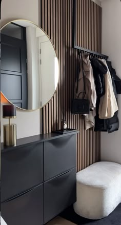 a room with a mirror, coat rack and stool next to a wall that has wooden slats on it