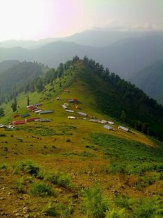 a grassy hill with houses on it and mountains in the background