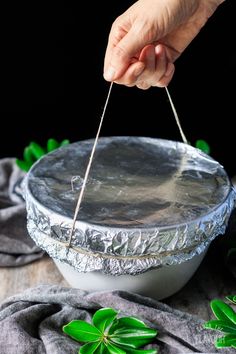 a person holding a stick over a tinfoil covered dish with leaves on the side